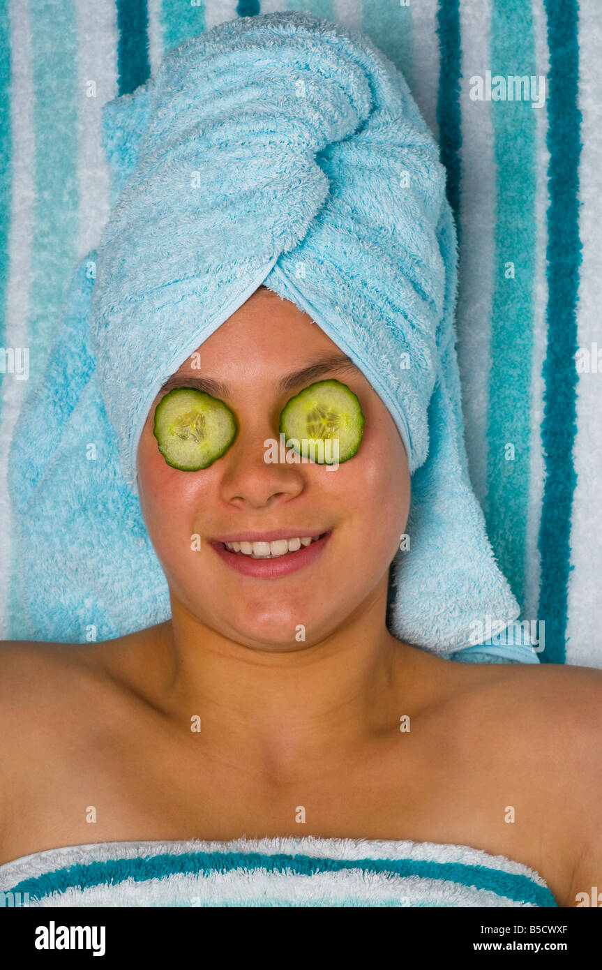 Una graziosa adolescente dà di sé un trattamento di bellezza ponendo le fette di cetriolo sopra i suoi occhi Foto Stock