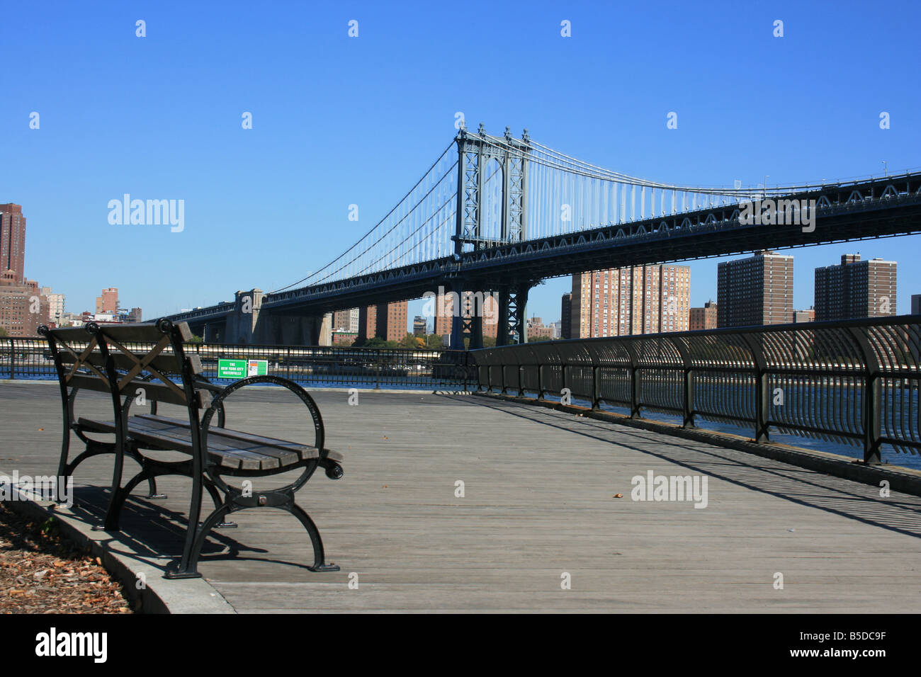 Una panchina nel parco lungo la East River a Brooklyn. Manhattan Bridge in background. Foto Stock
