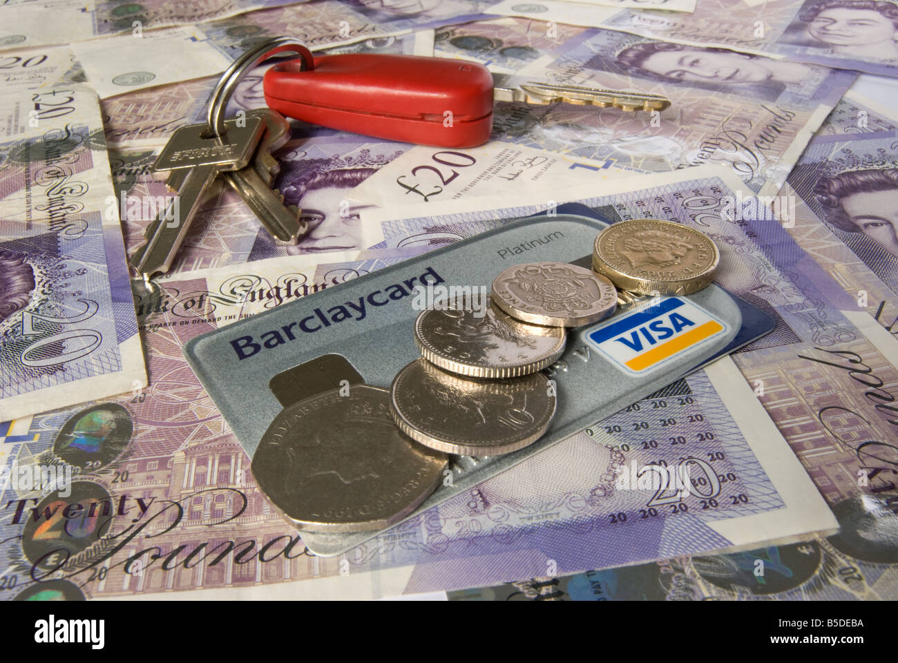 Chiavi auto carta di credito e monete su uno sfondo di venti pound note Foto Stock
