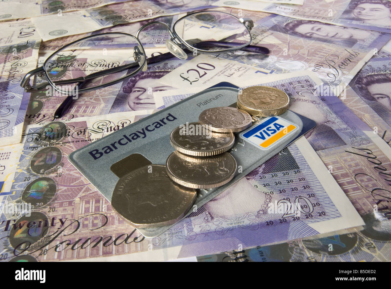 Bicchieri di carta di credito e monete su uno sfondo di venti pound note Foto Stock
