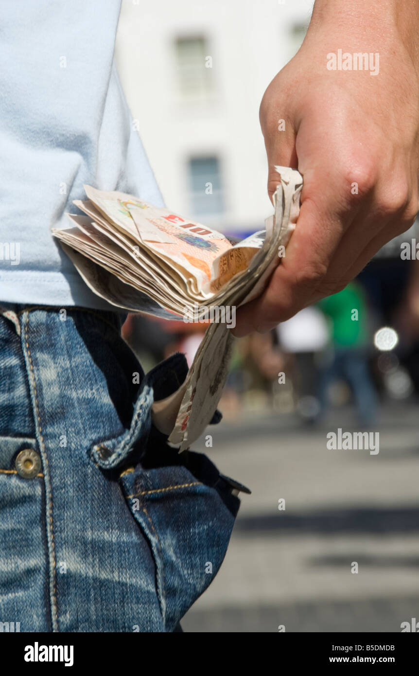 In prossimità di un lato di mettere un fascio di contanti in tasca posteriore di alcuni jeans Foto Stock