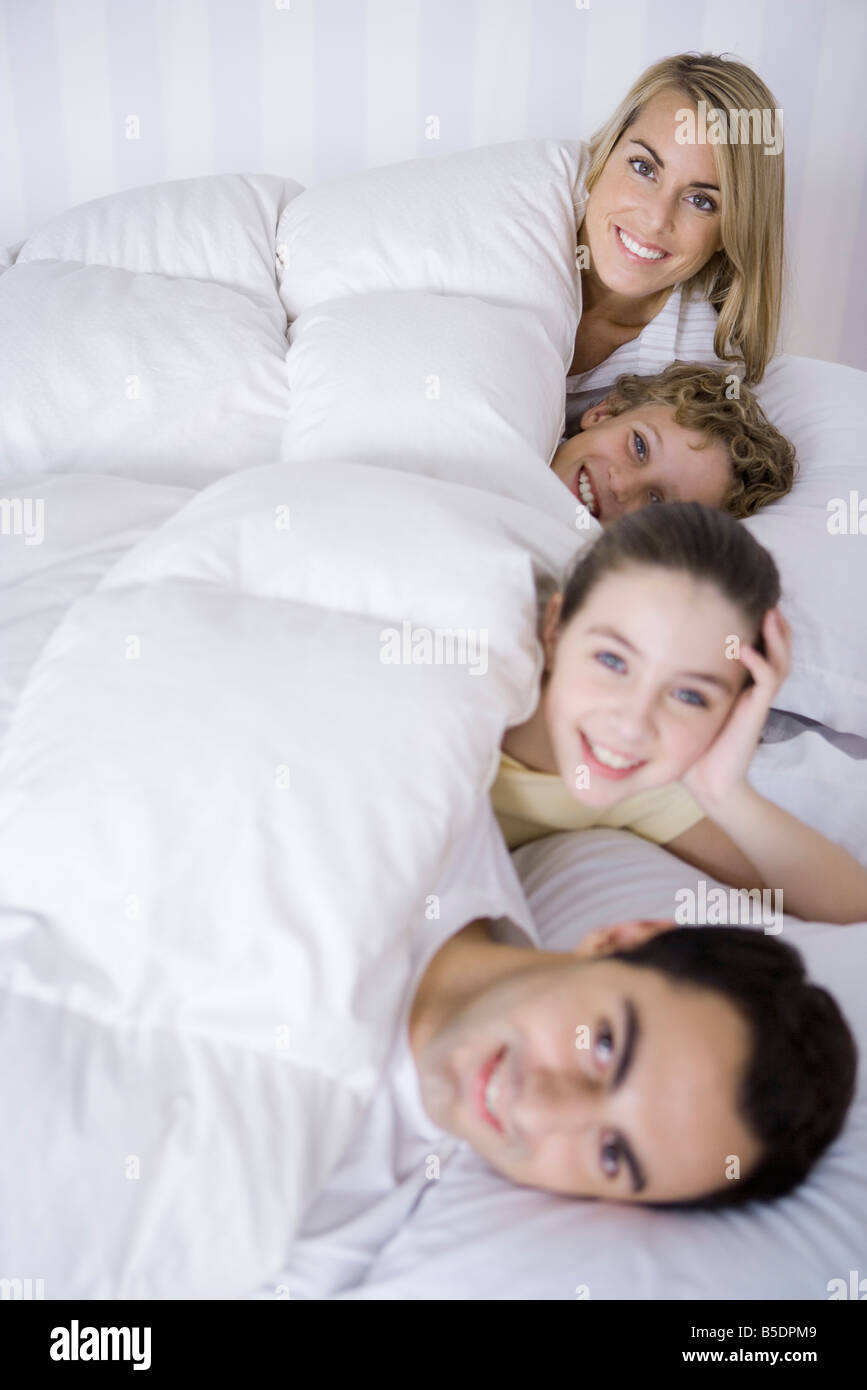 Famiglia giacente a letto insieme sorridente in telecamera Foto Stock