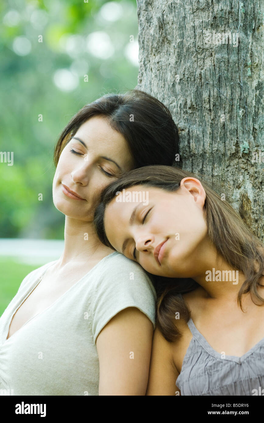 Madre e figlia teenager appoggiata contro l'albero con gli occhi chiusi, figlia di testa sulla madre di spallamento Foto Stock