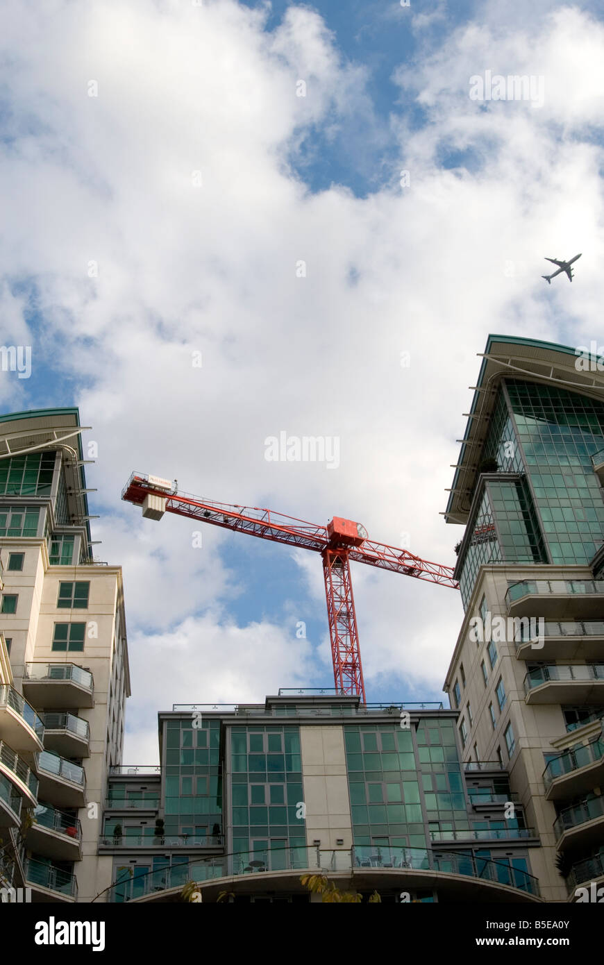 Un immagine guardando fino ad un moderno blocco di appartamenti a Londra con un aeroplano che vola al di sopra del cielo. Una grande gru rosse torri dietro. Foto Stock