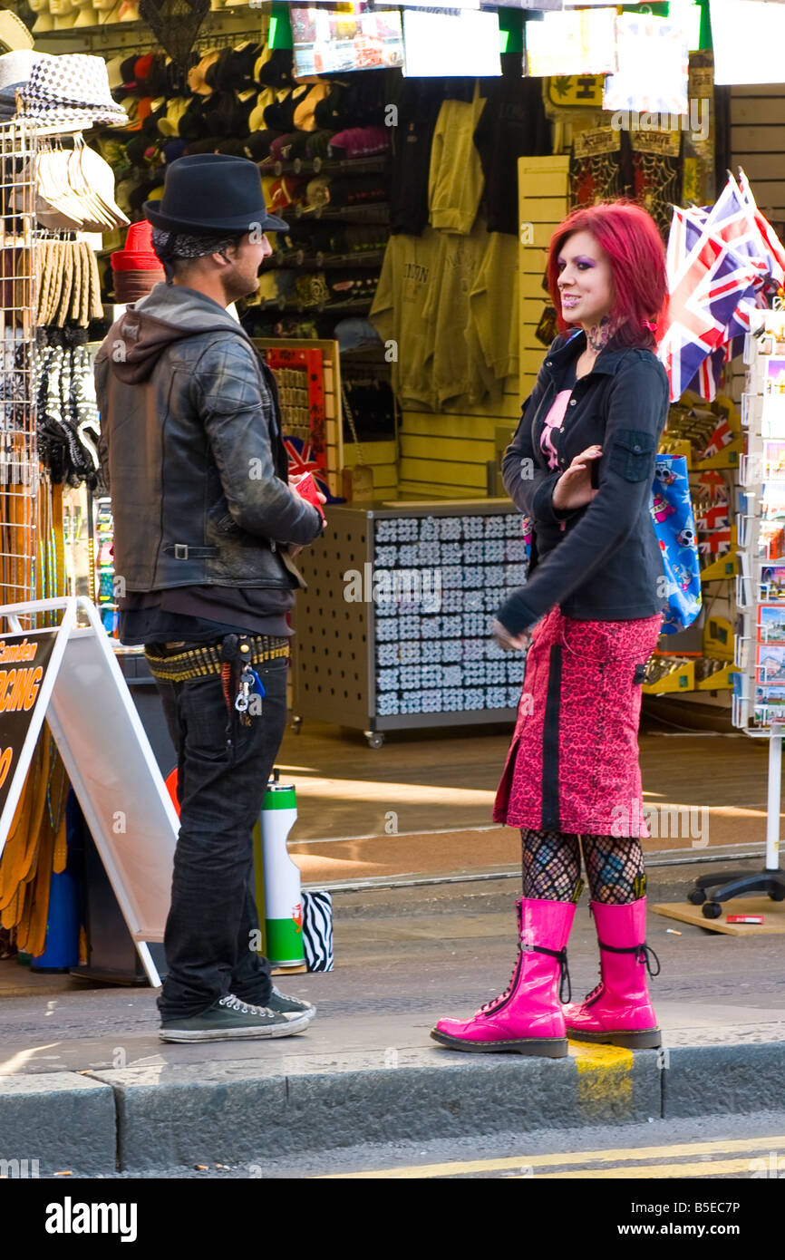 Londra , Camden Lock market bella femmina punk ragazza con i capelli rosa gonna , tattoo & legare stivali e faccia trafitto con ragazzo in hat Foto Stock