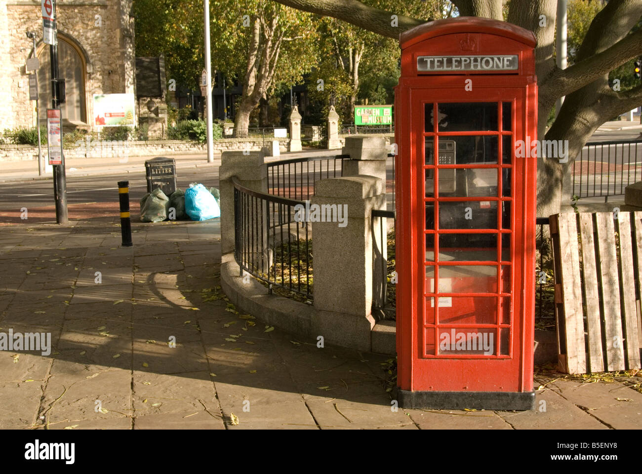 Uno stile vecchio telefono rosso box sorge su un percorso a Londra sul Tamigi la passerella. Un vecchio albero può essere visto crescere dietro Foto Stock