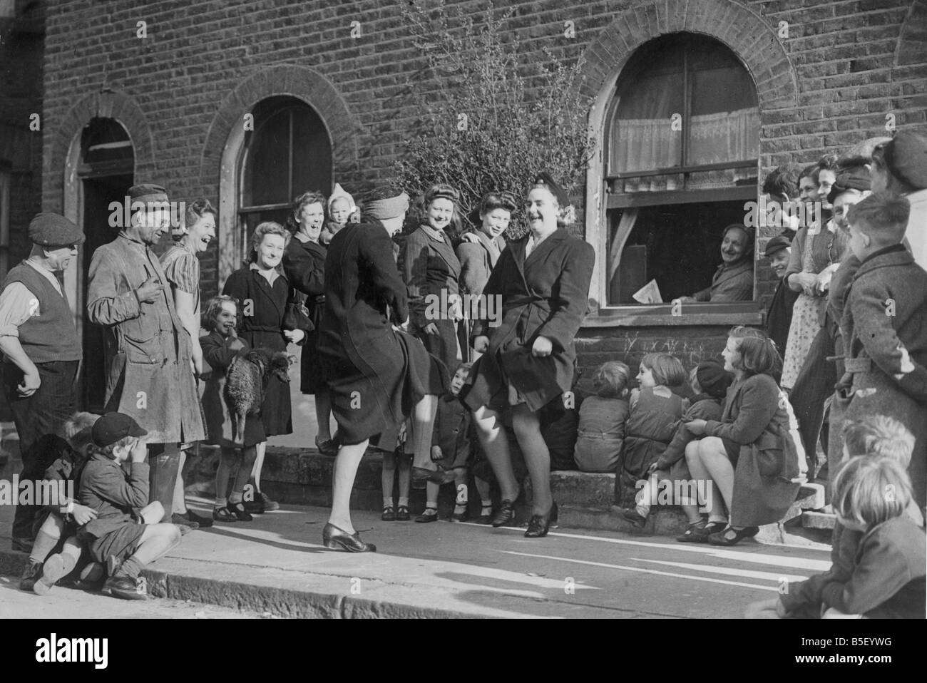 Una cinquantina di otto anni che Syd Landsdown, un riparatore di case bombardate durante la Seconda Guerra Mondiale, dà una improvvisata performance sul pianoforte per Londra le casalinghe e le loro famiglie come le folle si radunano per guardare le donne che danzano;Maggio 1945 Foto Stock