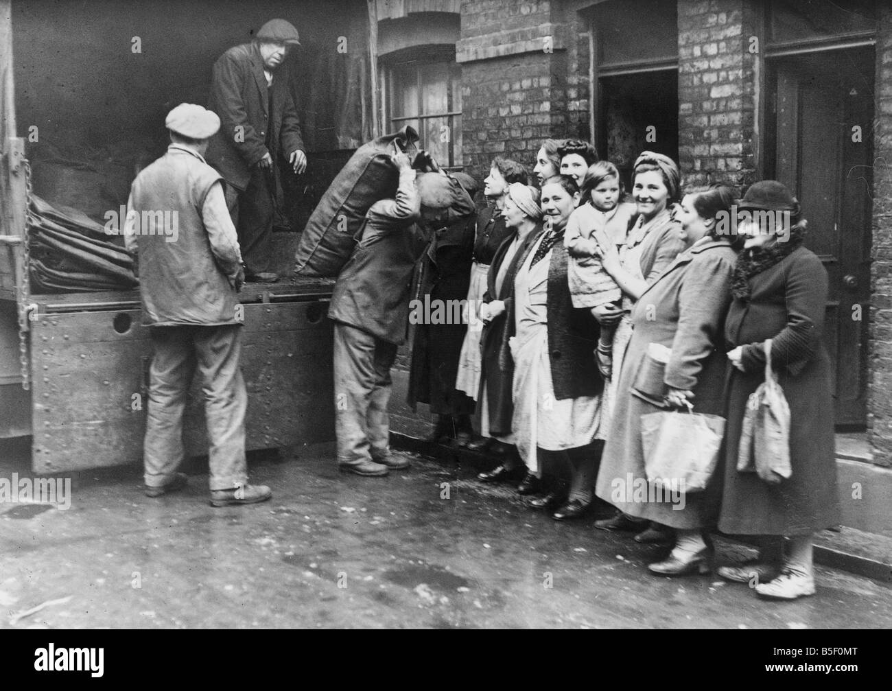 Londra casalinghe in coda fino a ricevere il loro approvvigionamento di carbone dal roundsman. Il coalman è stato fornito con un esercito autocarro Foto Stock