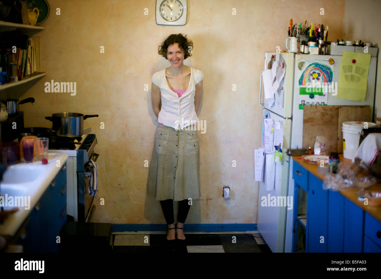 Ridendo donna sorride nello spazio negativo della sua cucina disordinato, sotto il cerchio del clock del viso. Tick tock... Foto Stock