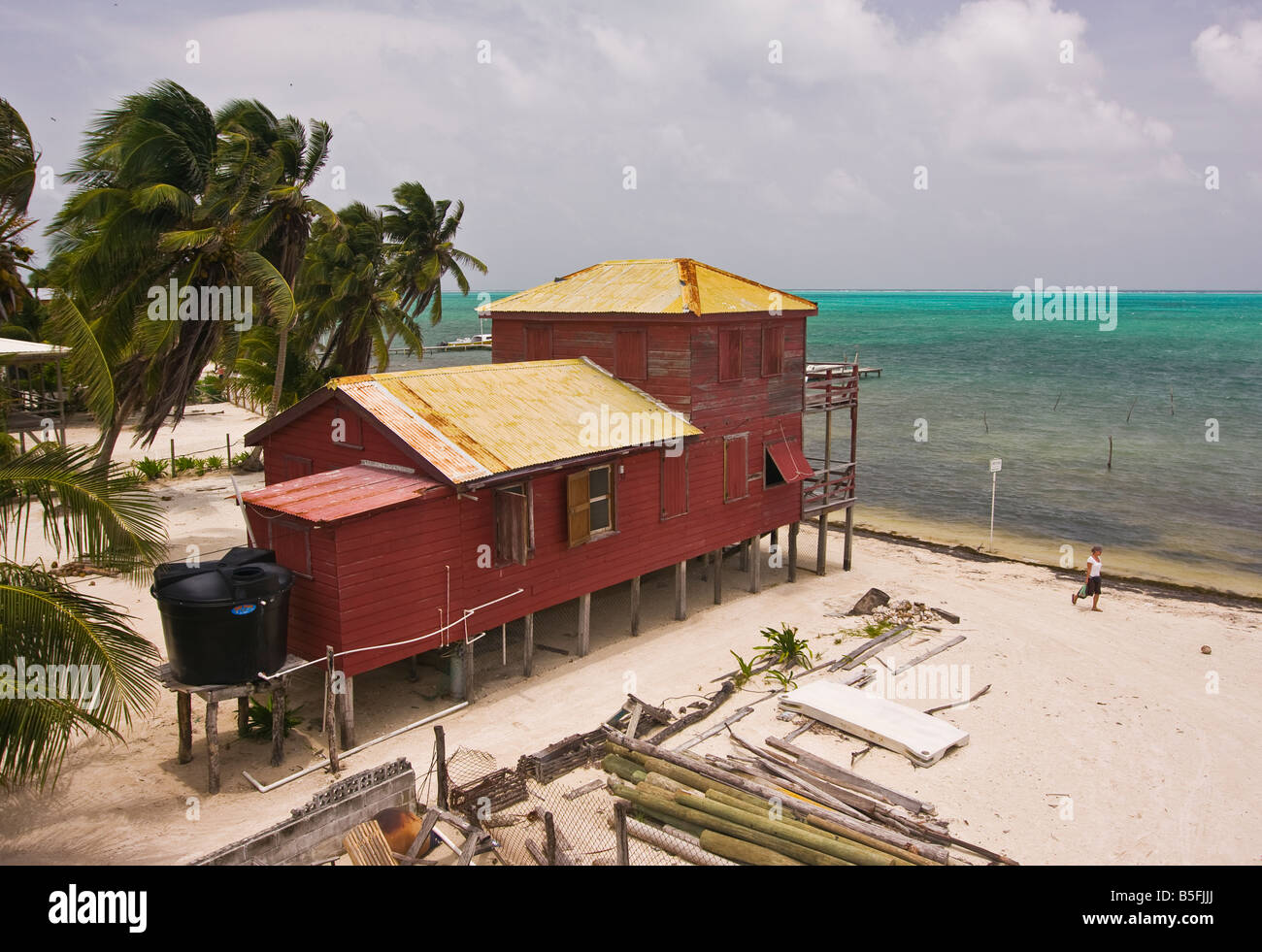 CAYE CAULKER BELIZE Tourist passeggiate lungo la spiaggia da casa su palafitte bacino di acqua sistema è sul retro del cottage a sinistra Foto Stock