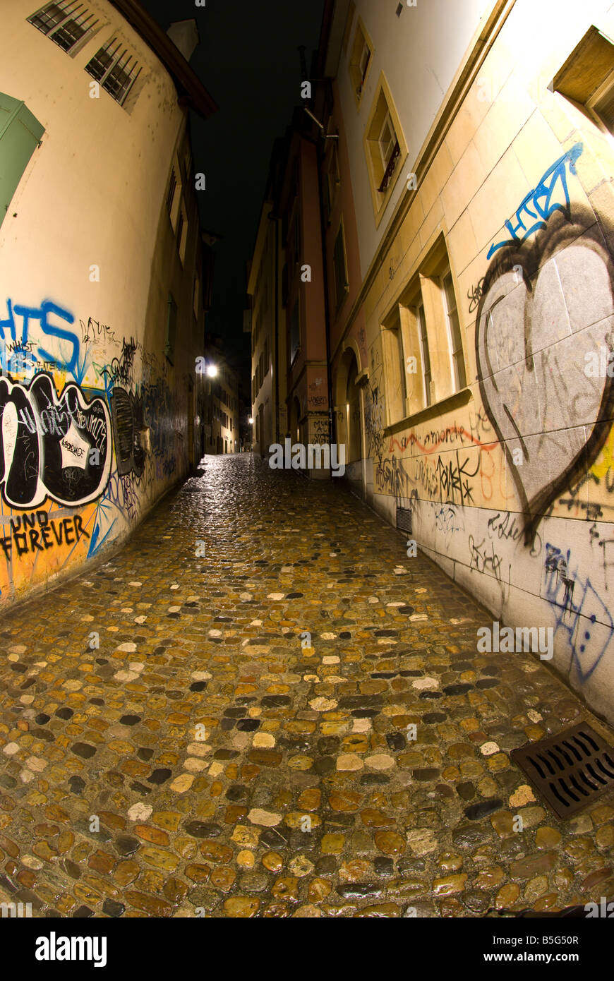 Un solitario e deserta città bagnata street riflettendo la luce da pioggia inzuppato acciottolato Foto Stock