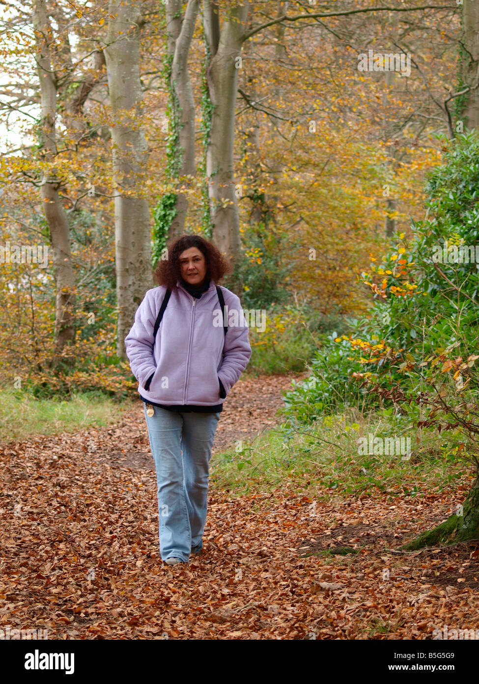30s donna con breve capelli ricci, camminando attraverso foglie secche che sono caduti gli alberi in un bosco. Autunno Foto Stock