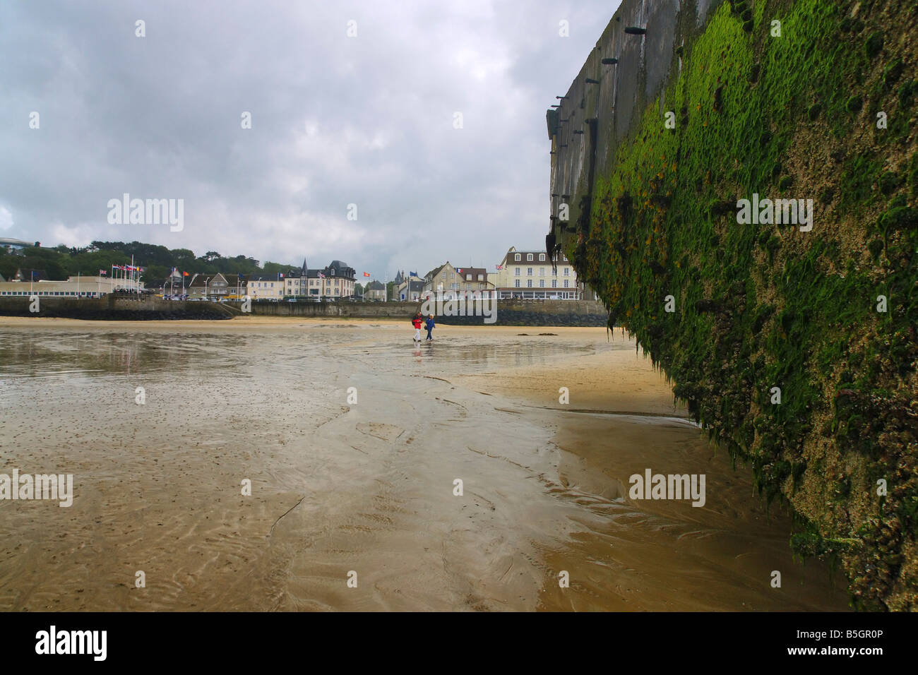 Arromanche,Normandia, Francia. Parte del "ulberry' porto artificiale dalla seconda guerra mondiale sulla spiaggia.La città è visto in background. Foto Stock