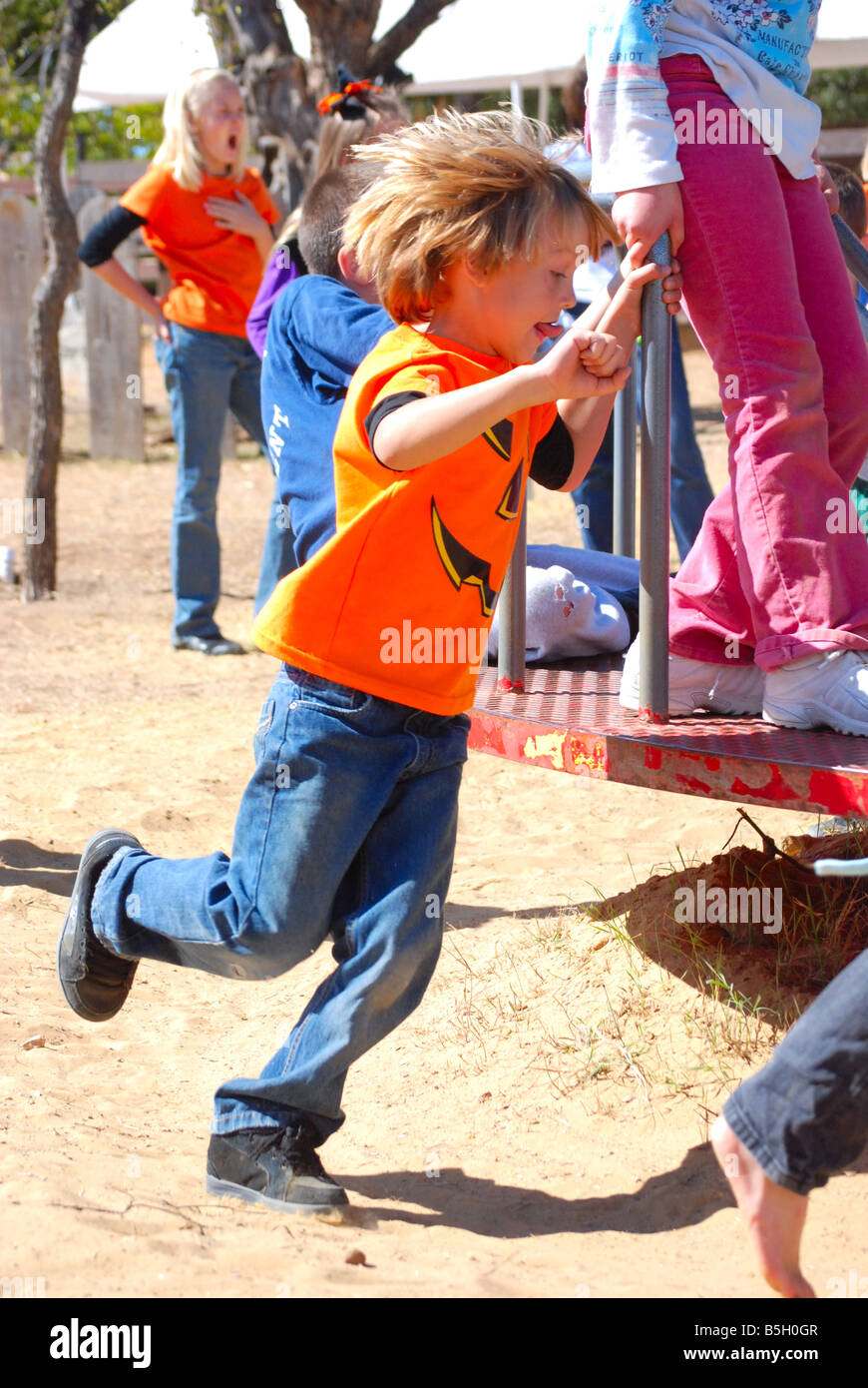 Little Boy racing al fianco di un merry-go-round su un parco giochi Foto Stock