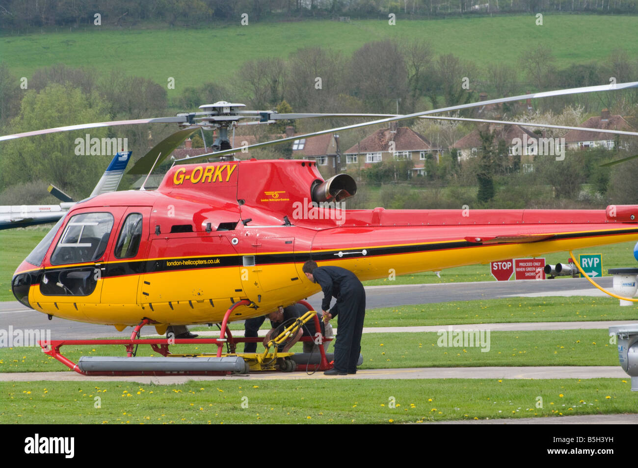 Riparazione meccanica lavorando su un rosso e giallo elicottero G ORKY aerodromo Redhill Surrey UK Elicotteri Foto Stock