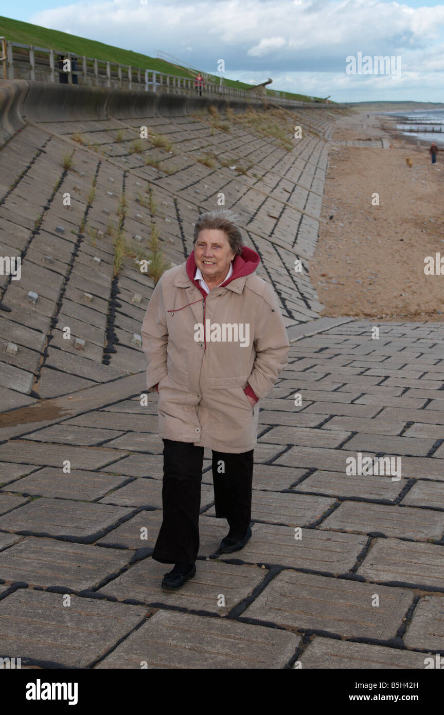 Signora anziana camminando sulla spiaggia di Aberdeen nel vento Scotland Regno Unito Foto Stock