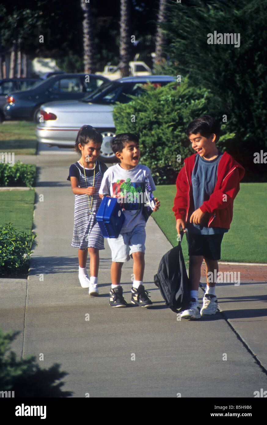 Tre bambini a piedi sul marciapiede come il loro ritorno a casa da scuola. Foto Stock