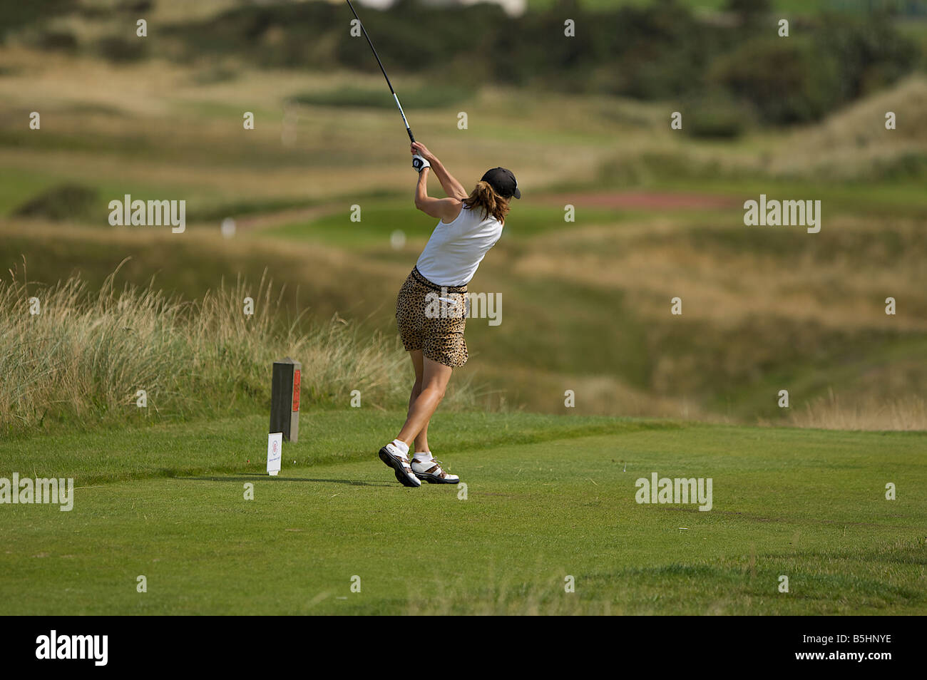 Signora golfista guida fuori colpendo il suo tiro lungo il fairway Foto Stock