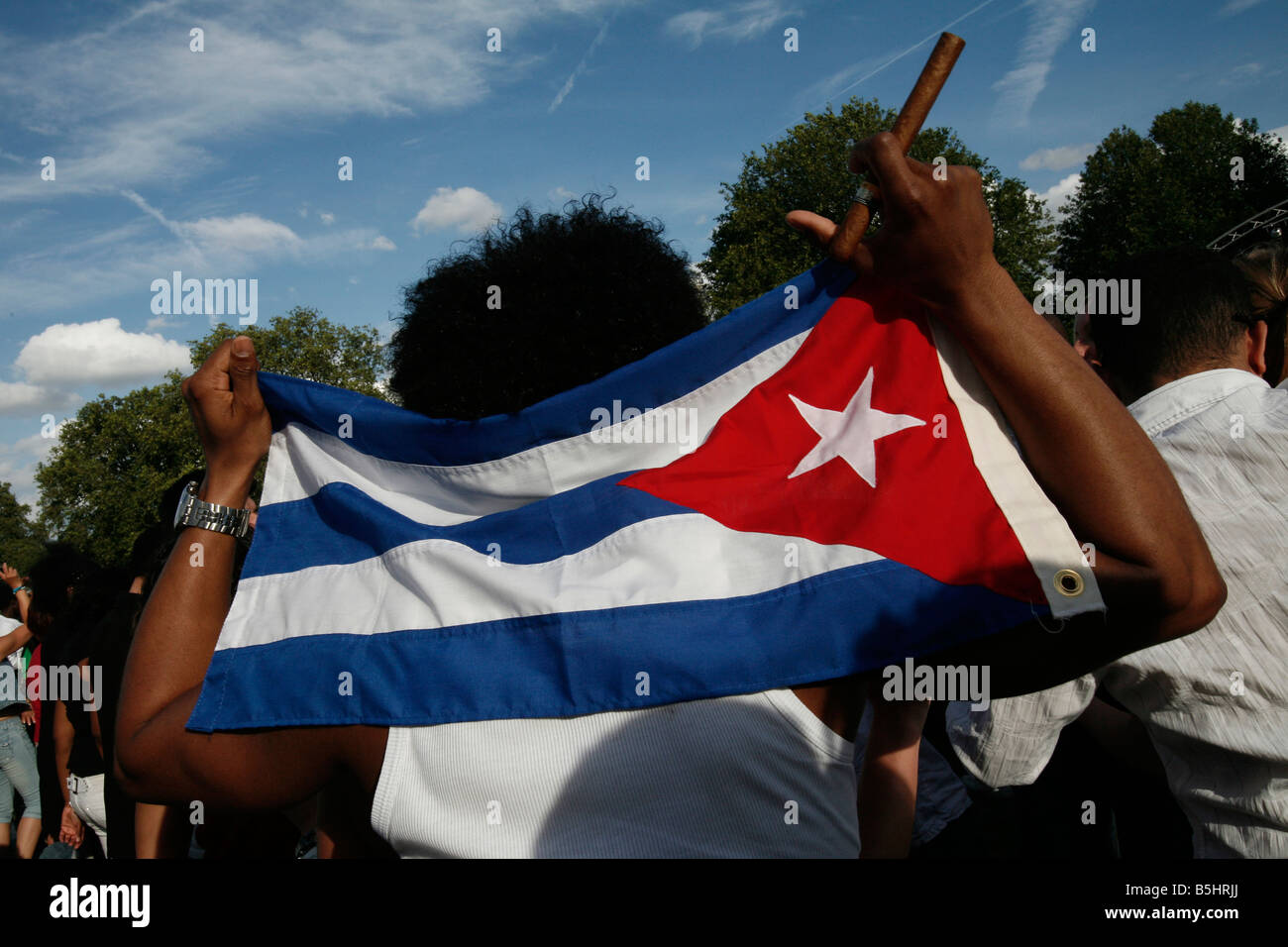 Uno spettatore con in mano una bandiera cubana mentre si tiene un sigaro cubano. Foto Stock