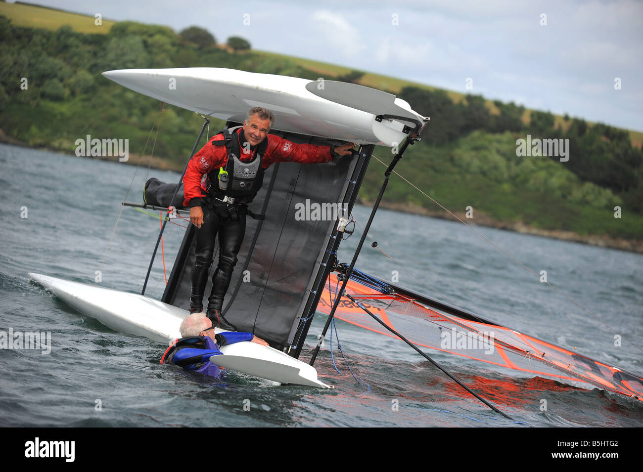 Due uomini cercando di destra un catamarano capovolto su un catamarano corso di conversione nella foto a Mylor porto vicino Falmouth Cornovaglia Foto Stock