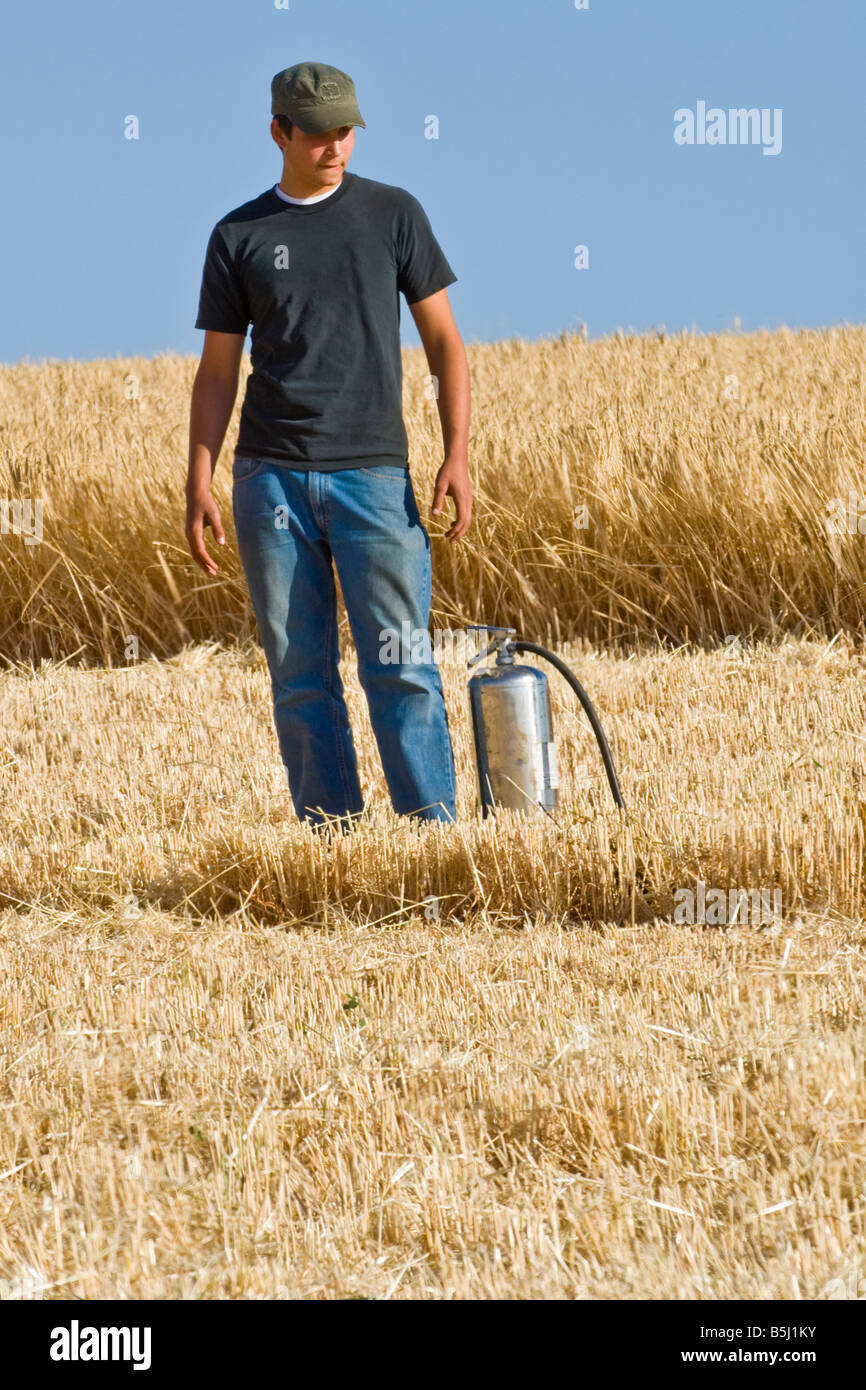 Un giovane bracciante agricolo sta guarda con un estintore in un campo di grano dopo un incendio incidente con una mietitrebbia Foto Stock