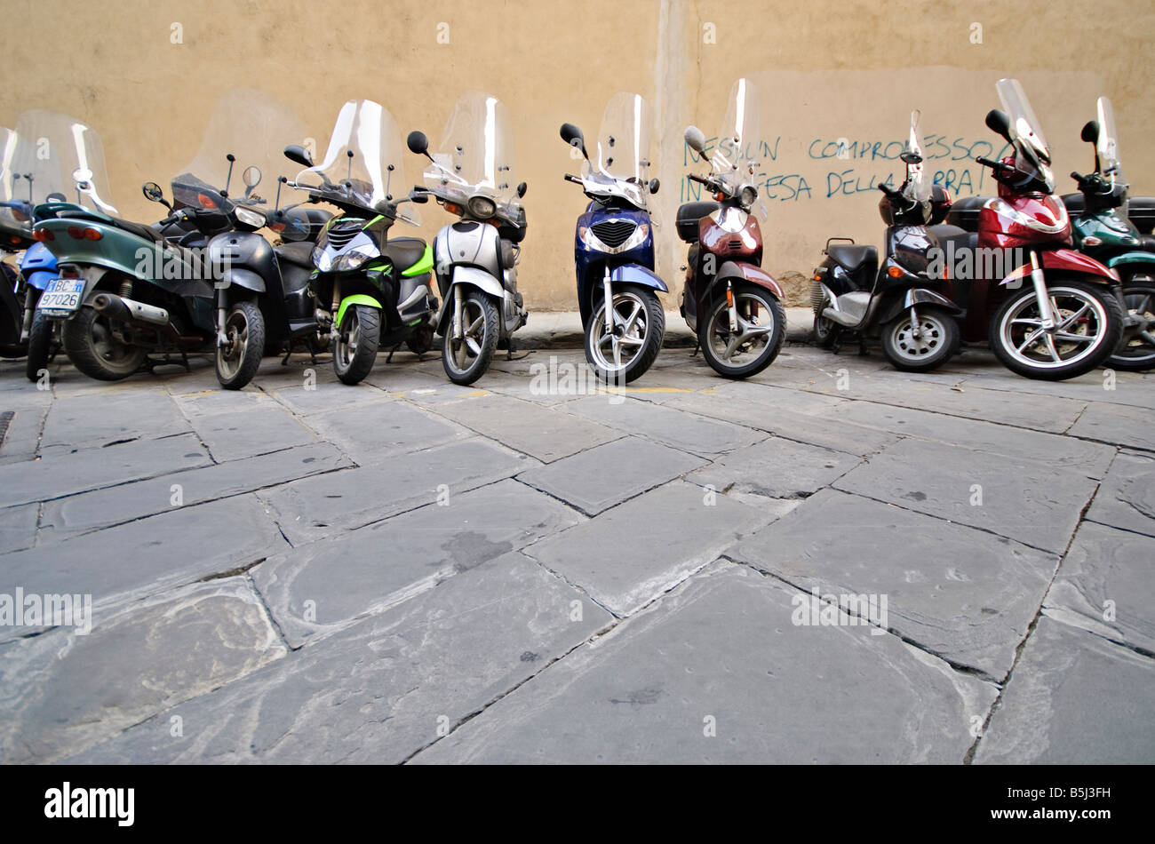 FIRENZE, Italia — Un mare di scooter e motociclette costeggia una stradina nel centro storico di Firenze. Le file strette di Vespe parcheggiate e altri motorini mostrano un aspetto quintessente della vita urbana italiana moderna sullo sfondo di un'architettura secolare. Foto Stock