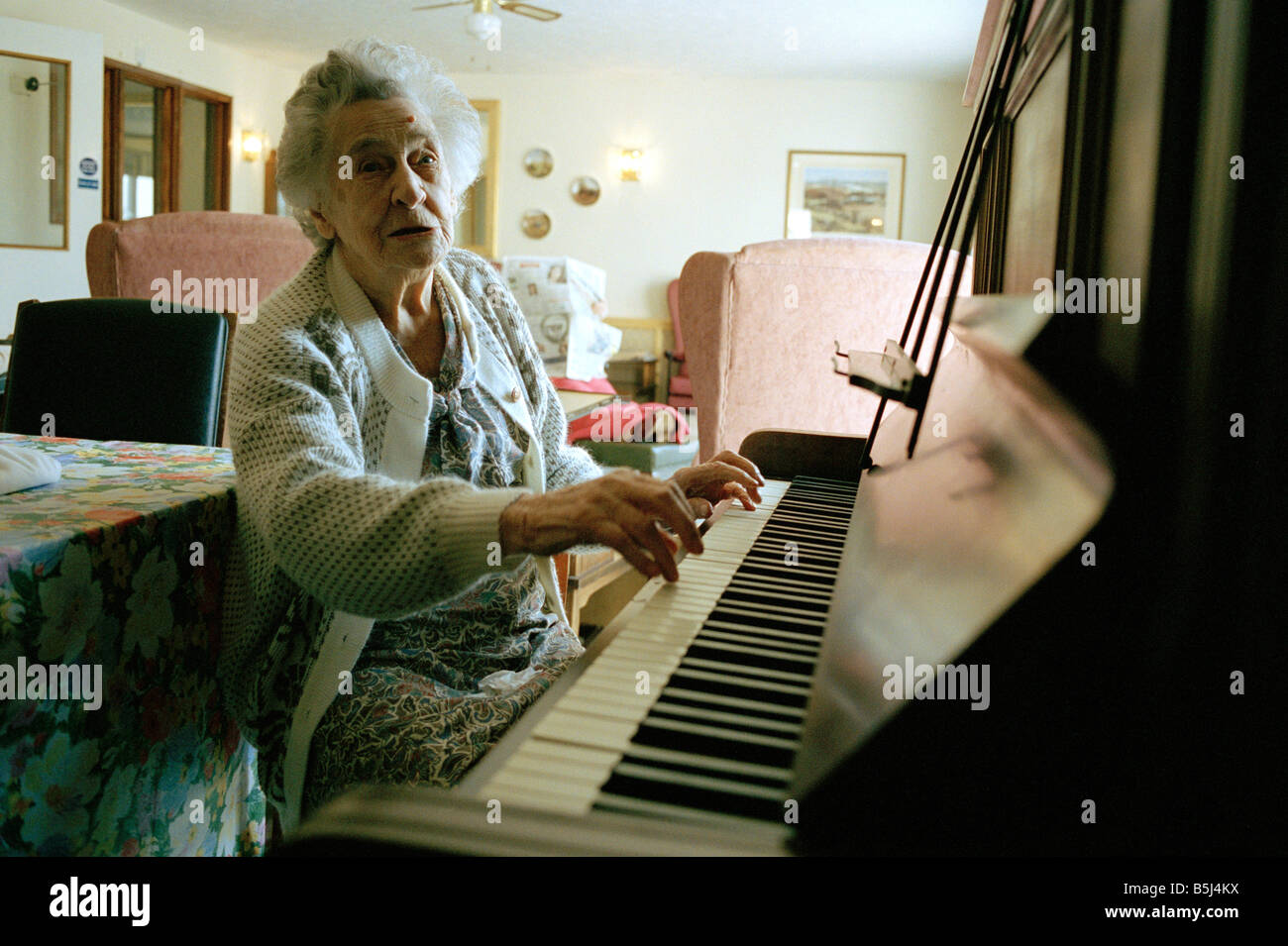 Anziano residente riproduzione di un pianoforte presso una casa di riposo in Inghilterra Foto Stock