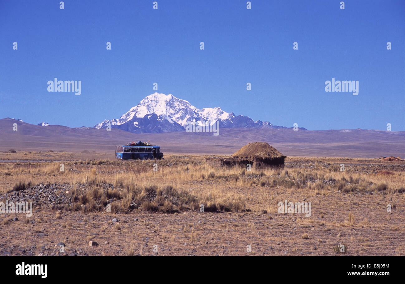 Bus locale la guida attraverso l'altiplano vicino a una capanna rustica, Mt Huayna Potosi in background, Bolivia Foto Stock