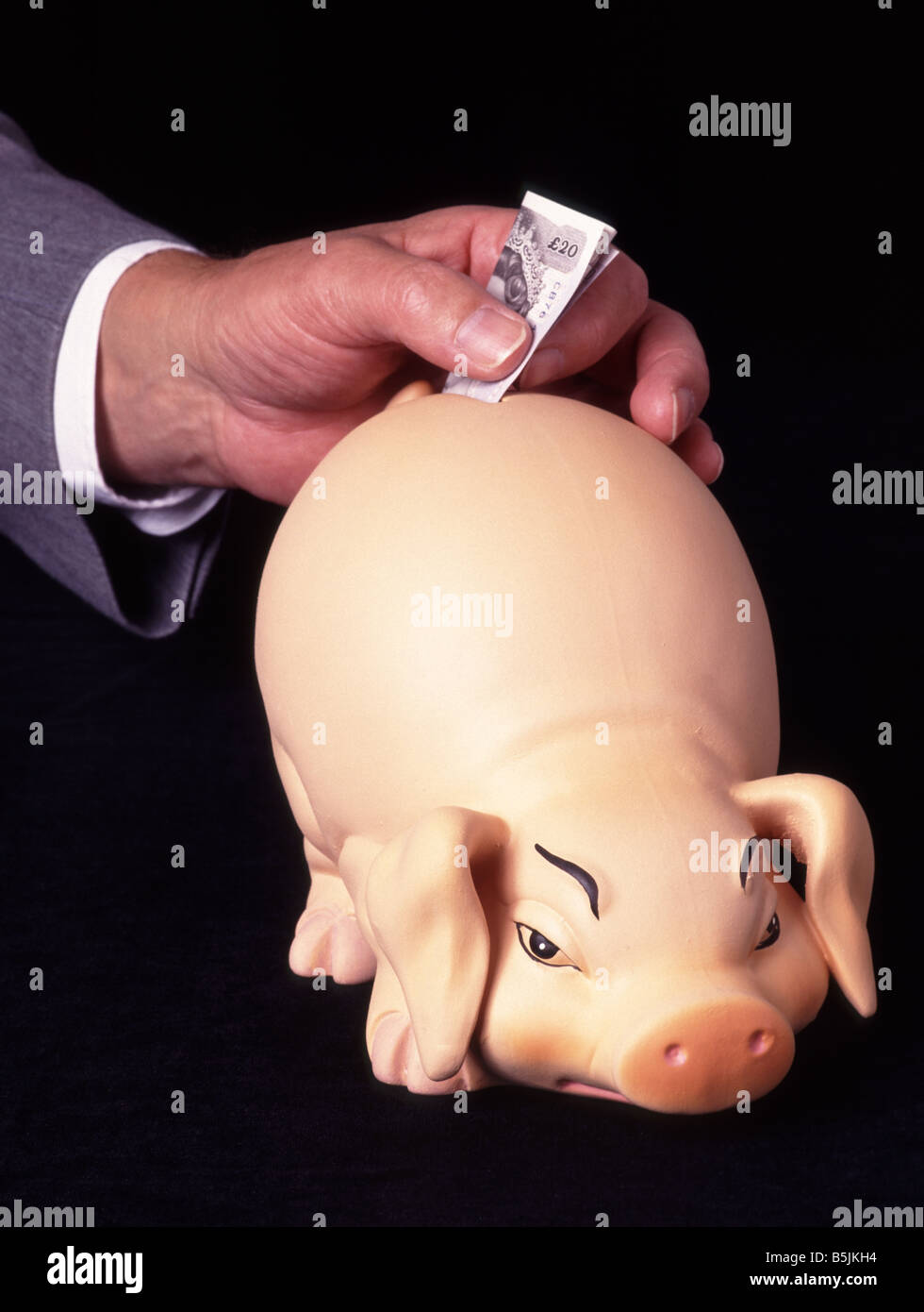Uomo che colloca una banconota da 20 sterline nella fessura di S Piggy Bank in ceramica, nota anche come una banca penny o una cassetta dei soldi nome tradizionale di un contenitore di monete Inghilterra Regno Unito Foto Stock