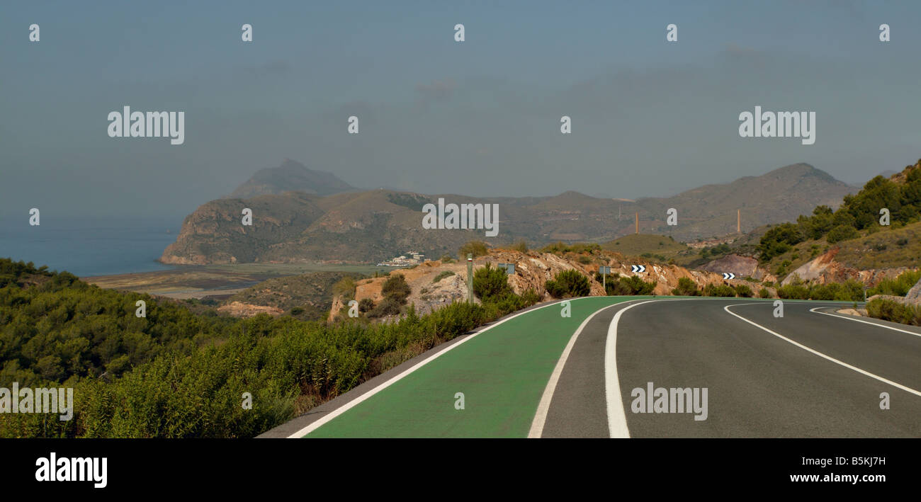 Una strada di guida nel sud della Spagna con una curva stretta a destra in avanti e un paesaggio aperto con una vista panoramica del mare sul lef Foto Stock