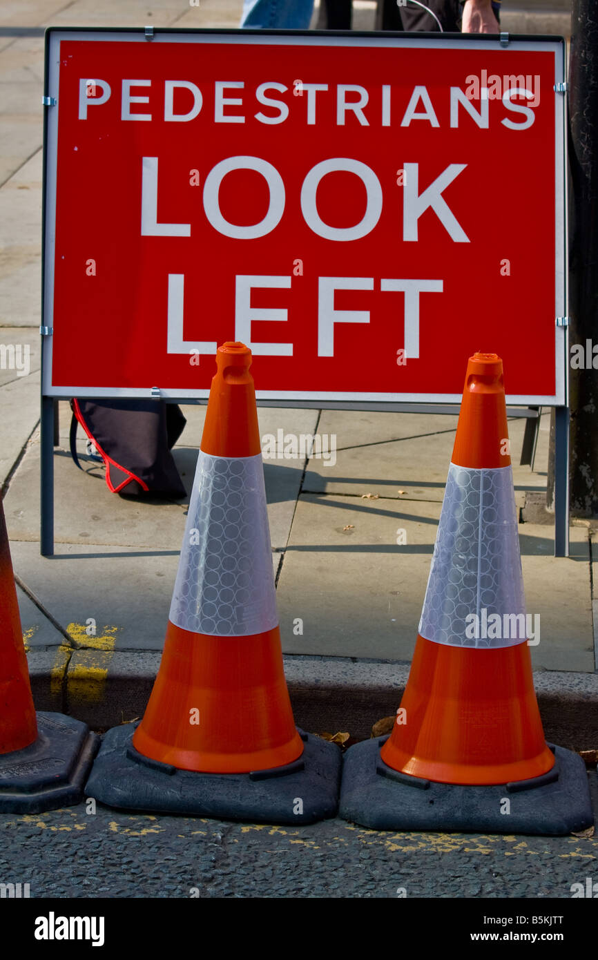 Un 'pedoni guardare a sinistra" cartello stradale con dei coni di fronte ad esso. Foto Stock
