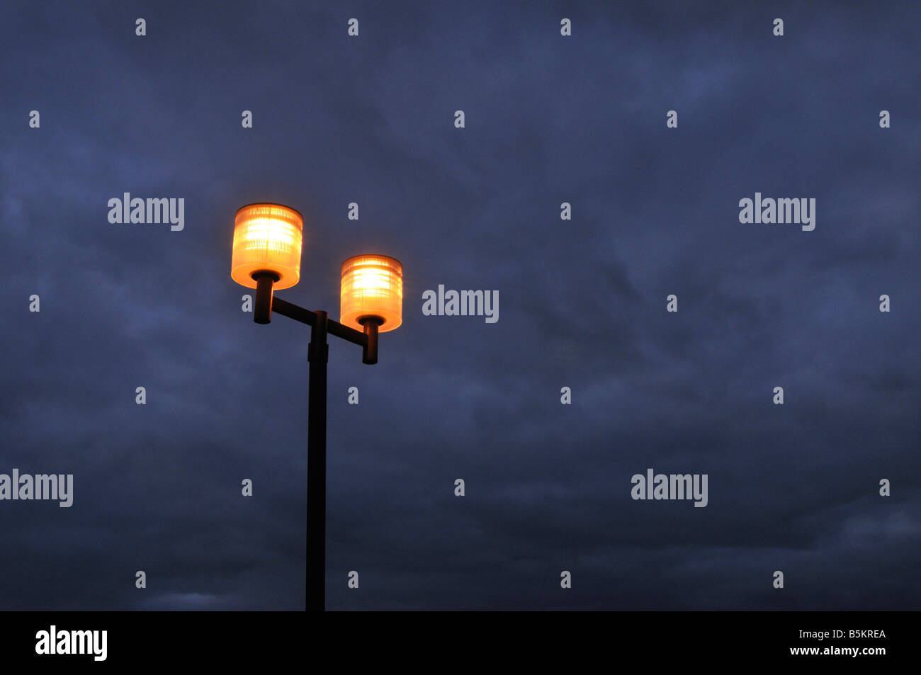 Drammatica eerie parcheggio lampioni al crepuscolo contro blu grigio nuvoloso cielo notturno Foto Stock