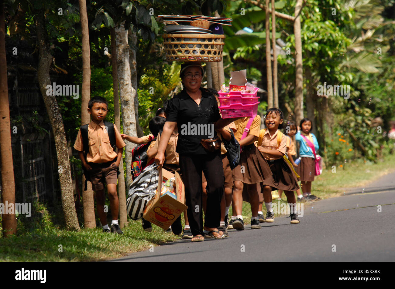 Signora Balinese con snack per la vendita e la scuola i bambini corrono al suo, Bali, Indonesia Foto Stock