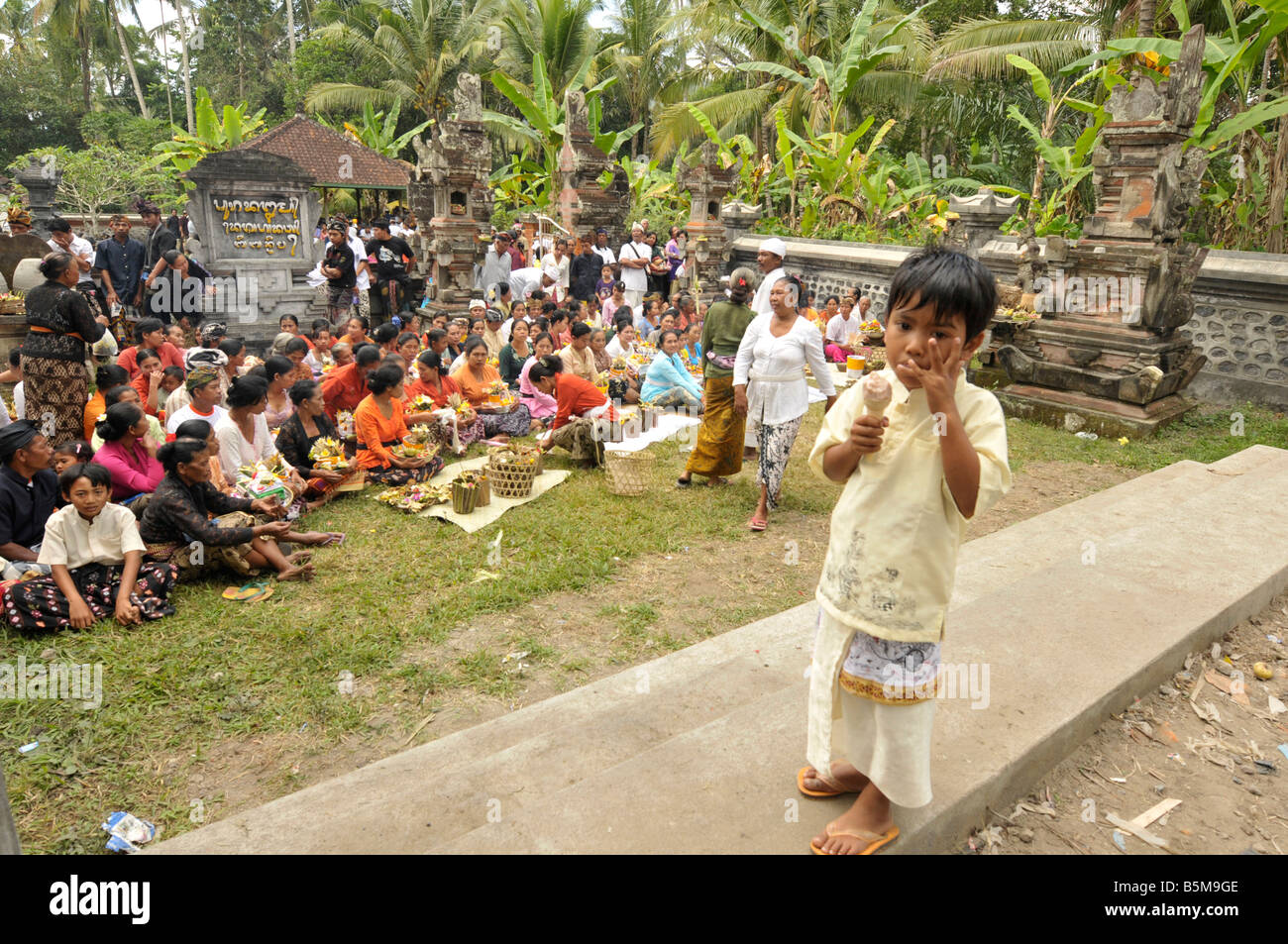 Ragazzo Balinese mangiare gelato alla cerimonia di cremazione, Bali, Indonesia Foto Stock
