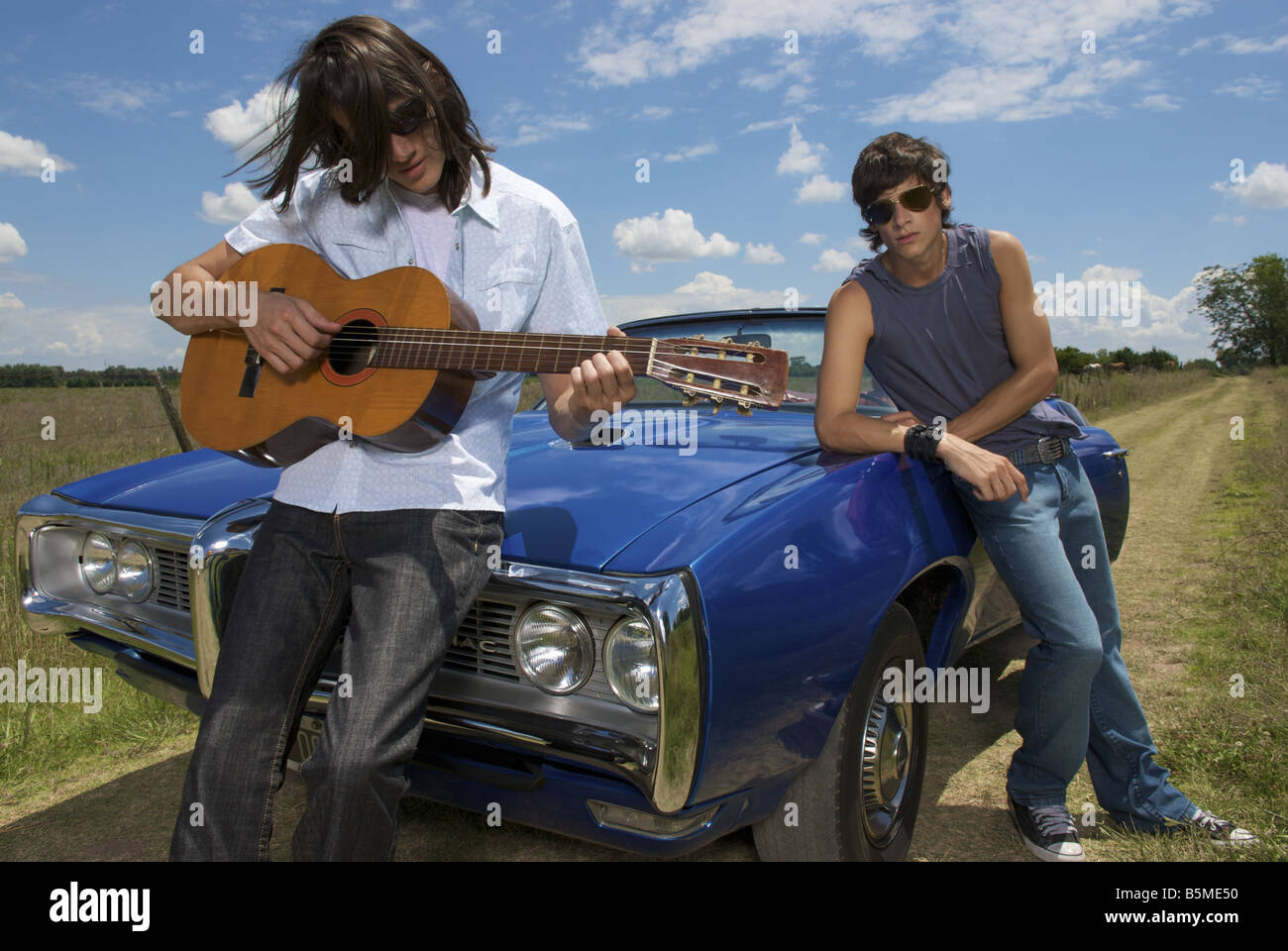 Due maschi appoggiata contro un auto e suonare la chitarra. Foto Stock