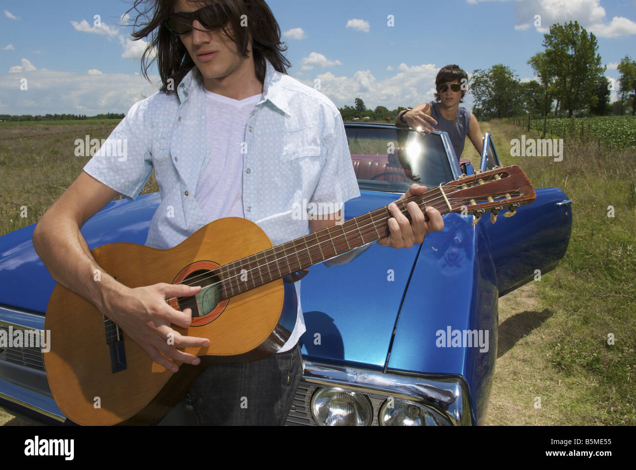 Due maschi con un auto blu e a suonare la chitarra Foto Stock