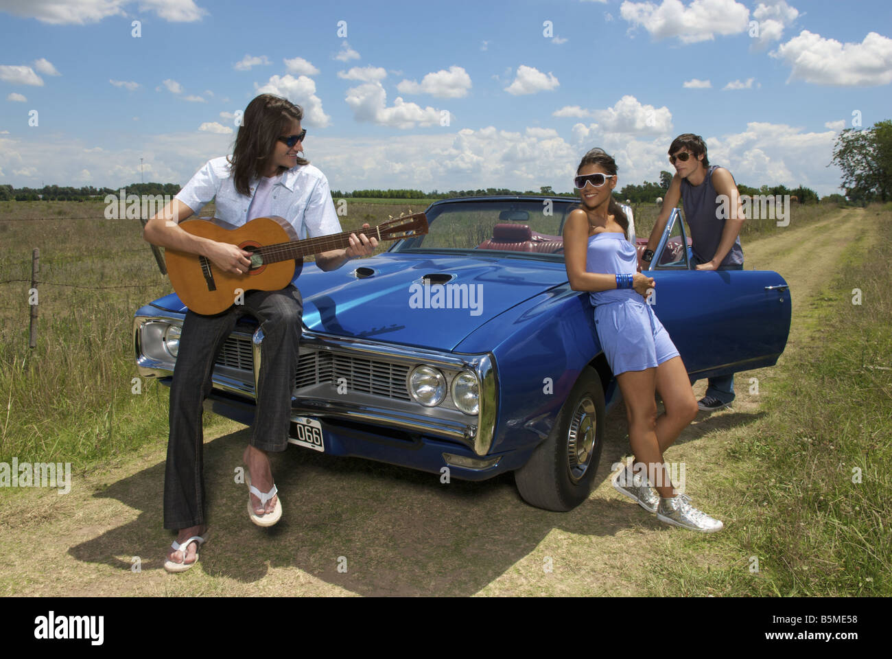 Tre giovani adulti con un auto blu a suonare la chitarra Foto Stock