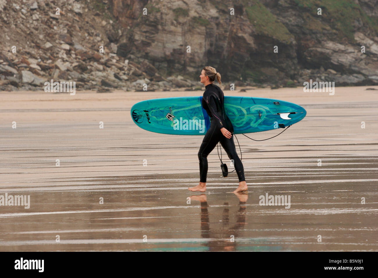 Ragazza del surfista camminando giù in spiaggia a Watergate Bay North Cornwall Foto Stock