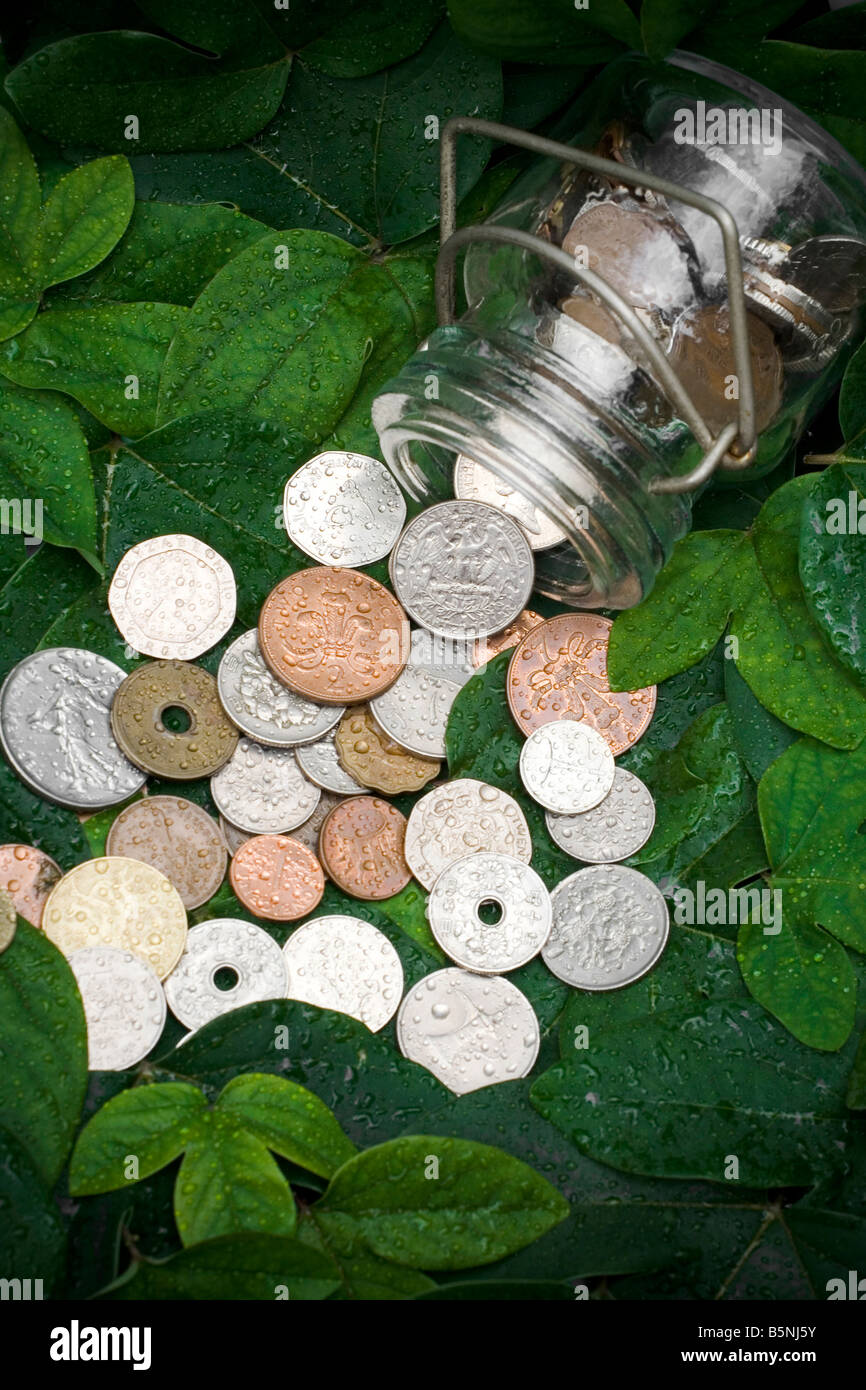 Monete antiche si versato da un contenitore di vetro su foglie verdi Foto Stock