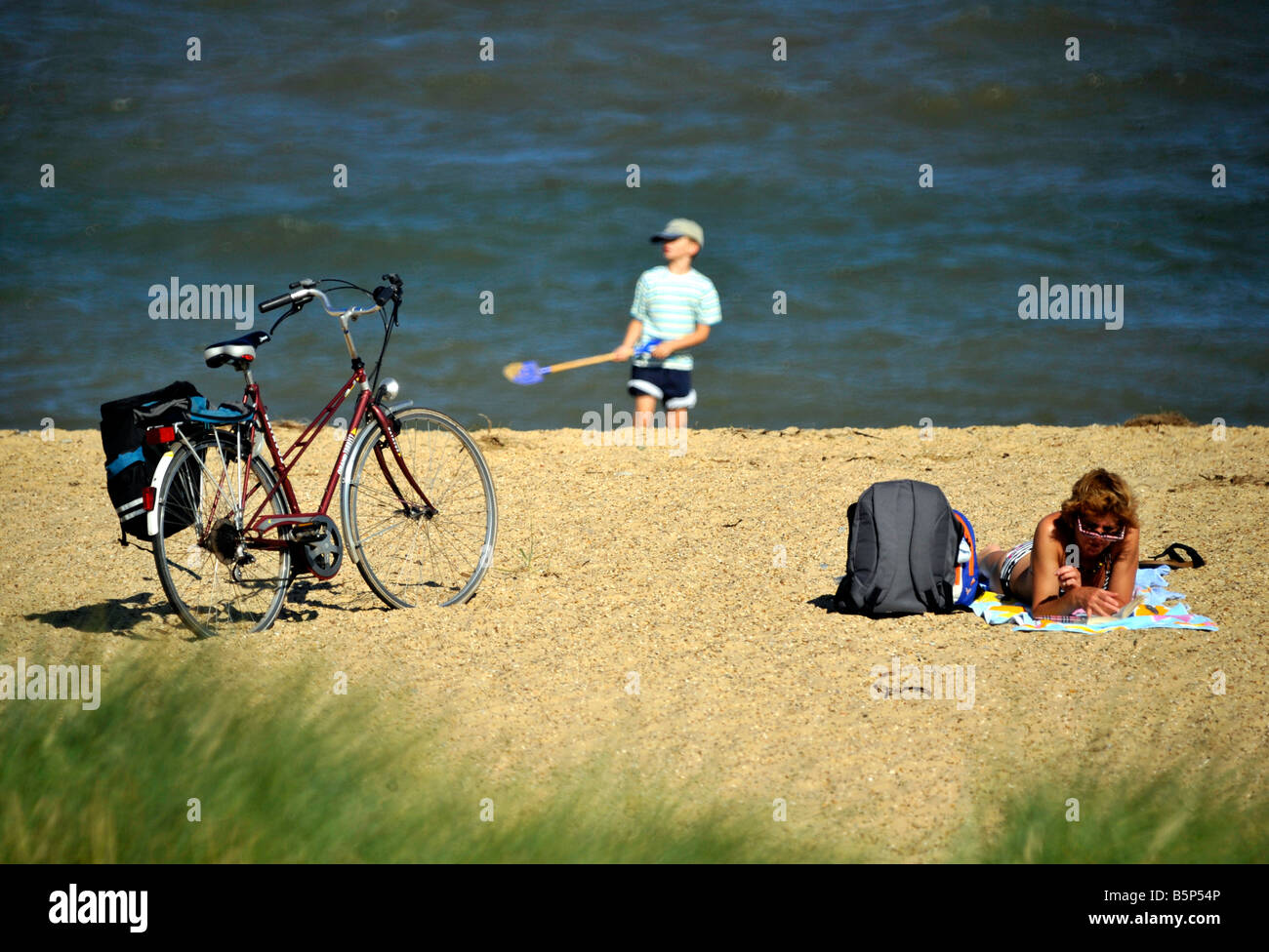 Donna rilassante sulla spiaggia mentre giovane ragazzo gioca in sabbia con una vanga Foto Stock