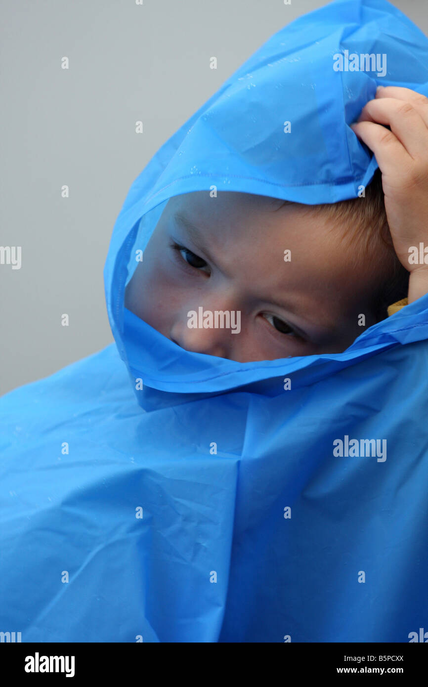 Un giovane bambino alle prese con una pioggia blu poncho o giacca Foto Stock