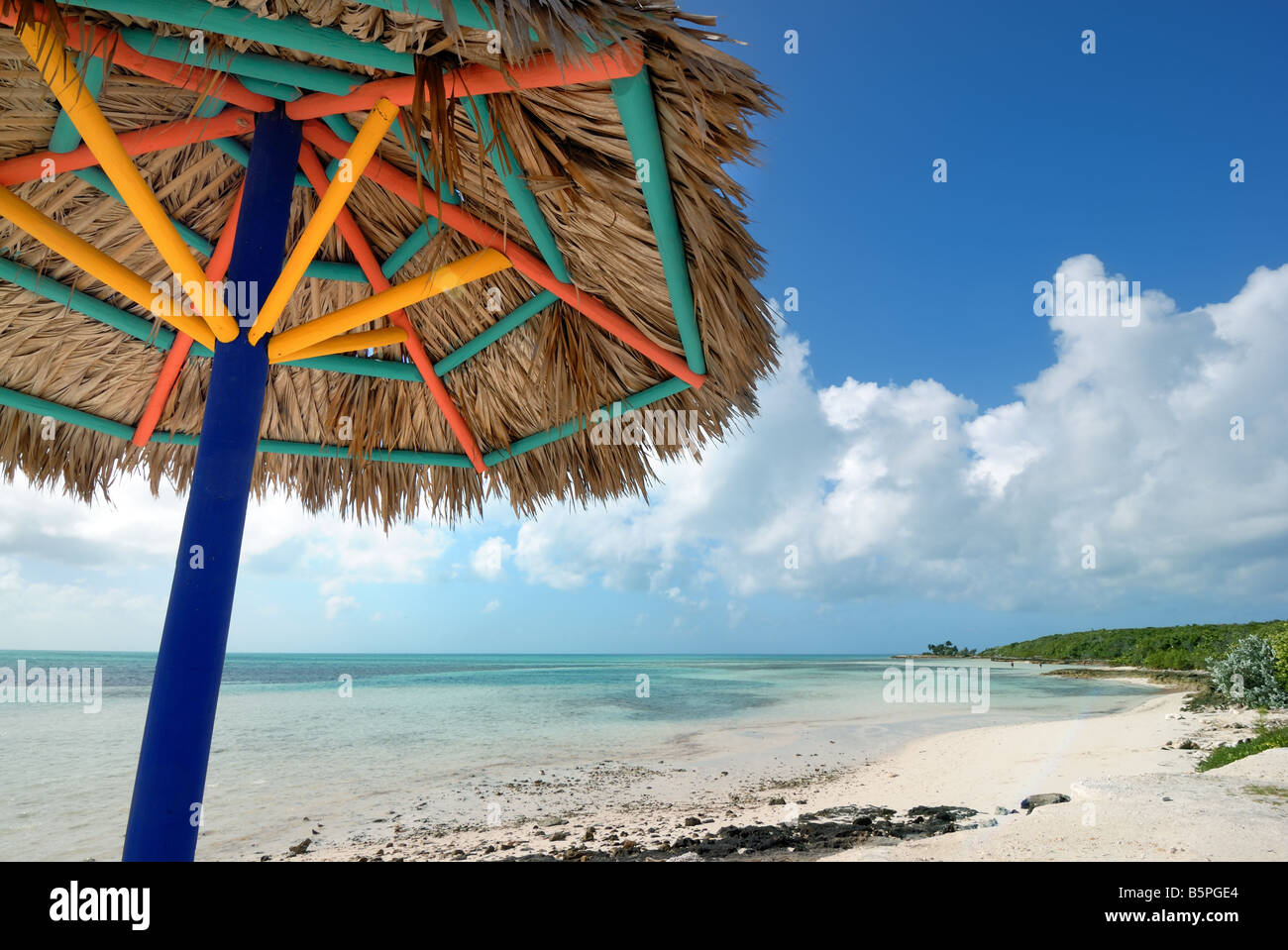 Un colorato ombrellone di paglia su una spiaggia deserta su Little Staffili Cay, Bahamas. Foto Stock