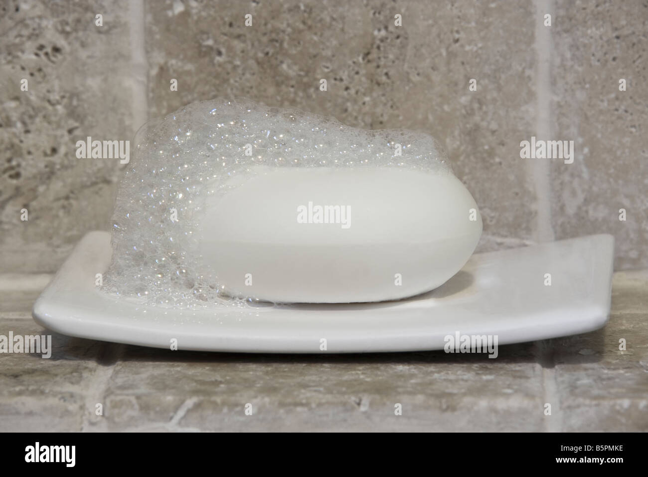 Barra di sapone con schiuma su un piatto contro una pietra parete piastrellata Foto Stock