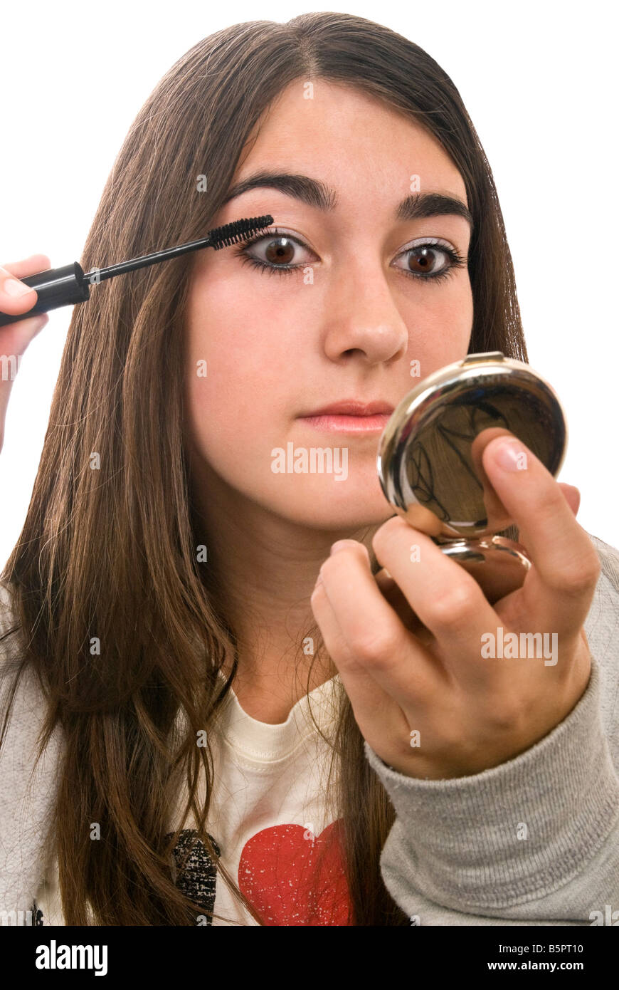 Ritratto verticale di una giovane ragazza adolescente mettendo su make up prima che ella si spegne contro uno sfondo bianco Foto Stock