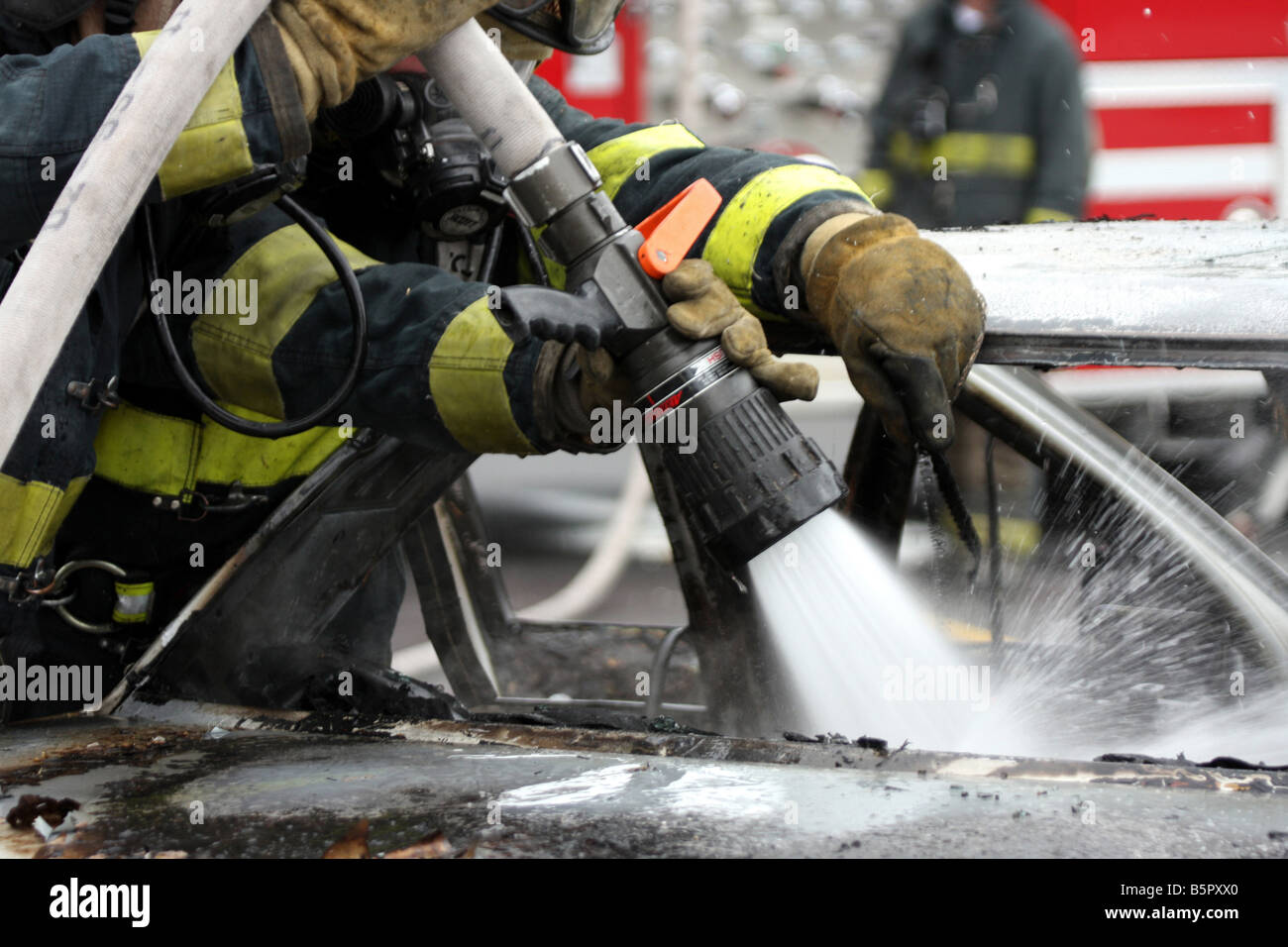 Tre vigili del fuoco messa fuori una macchina fuoco con un vigile del fuoco rivolto a un hot spot che ha bisogno di acqua per spegnere Foto Stock