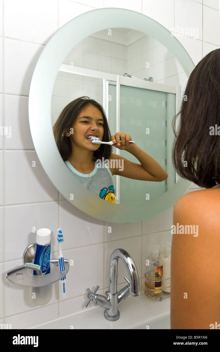 Ritratto verticale di una giovane ragazza la pulizia i suoi denti con uno spazzolino da denti riflessa in uno specchio del bagno. Foto Stock
