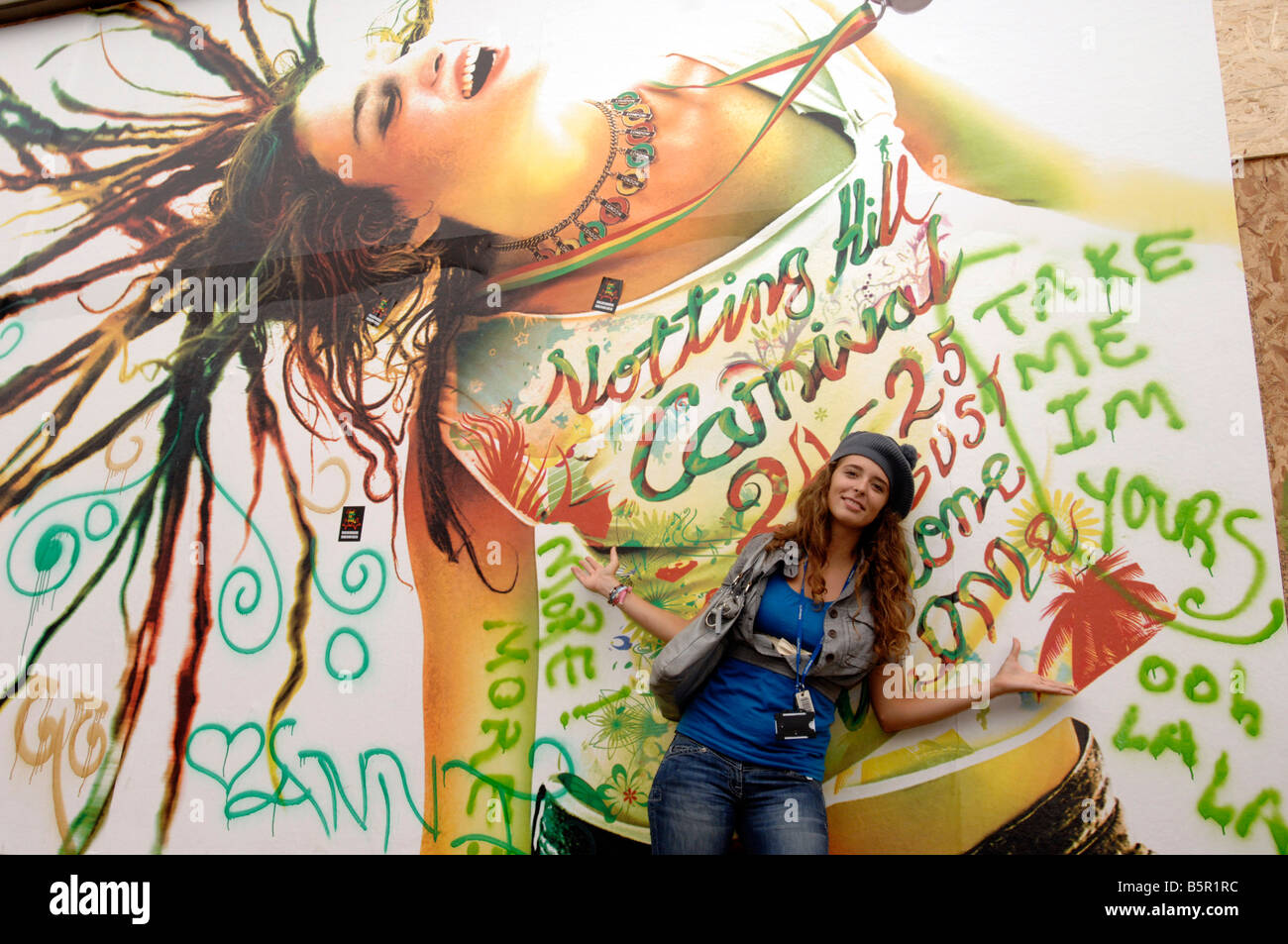 Un modello pone di fronte a enormi poster per celebrare Londra il carnevale di Notting Hill Foto Stock