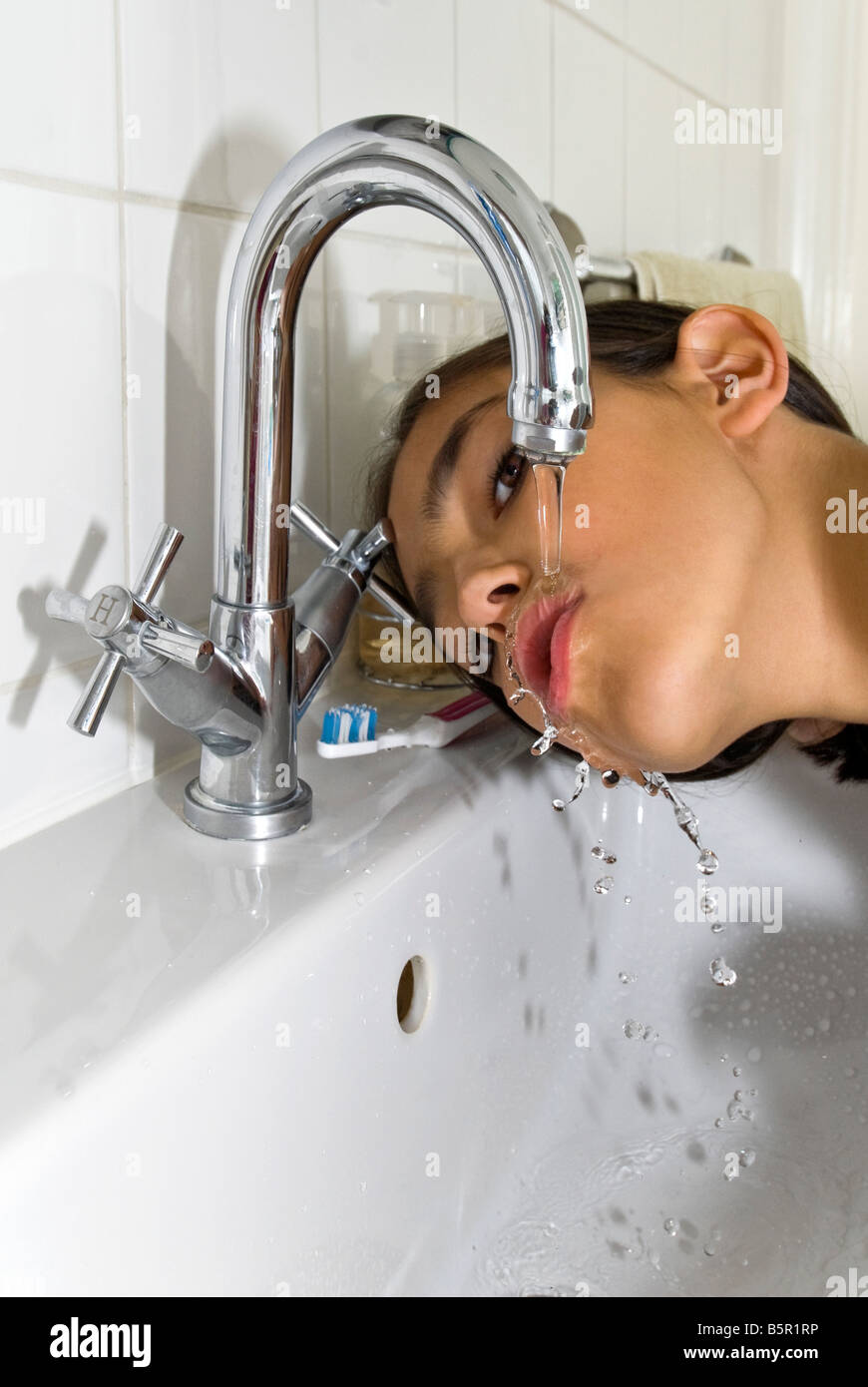 Ritratto verticale di una giovane ragazza di bere un po' d'acqua da un rubinetto miscelatore dopo la spazzolatura i suoi denti nella stanza da bagno Foto Stock