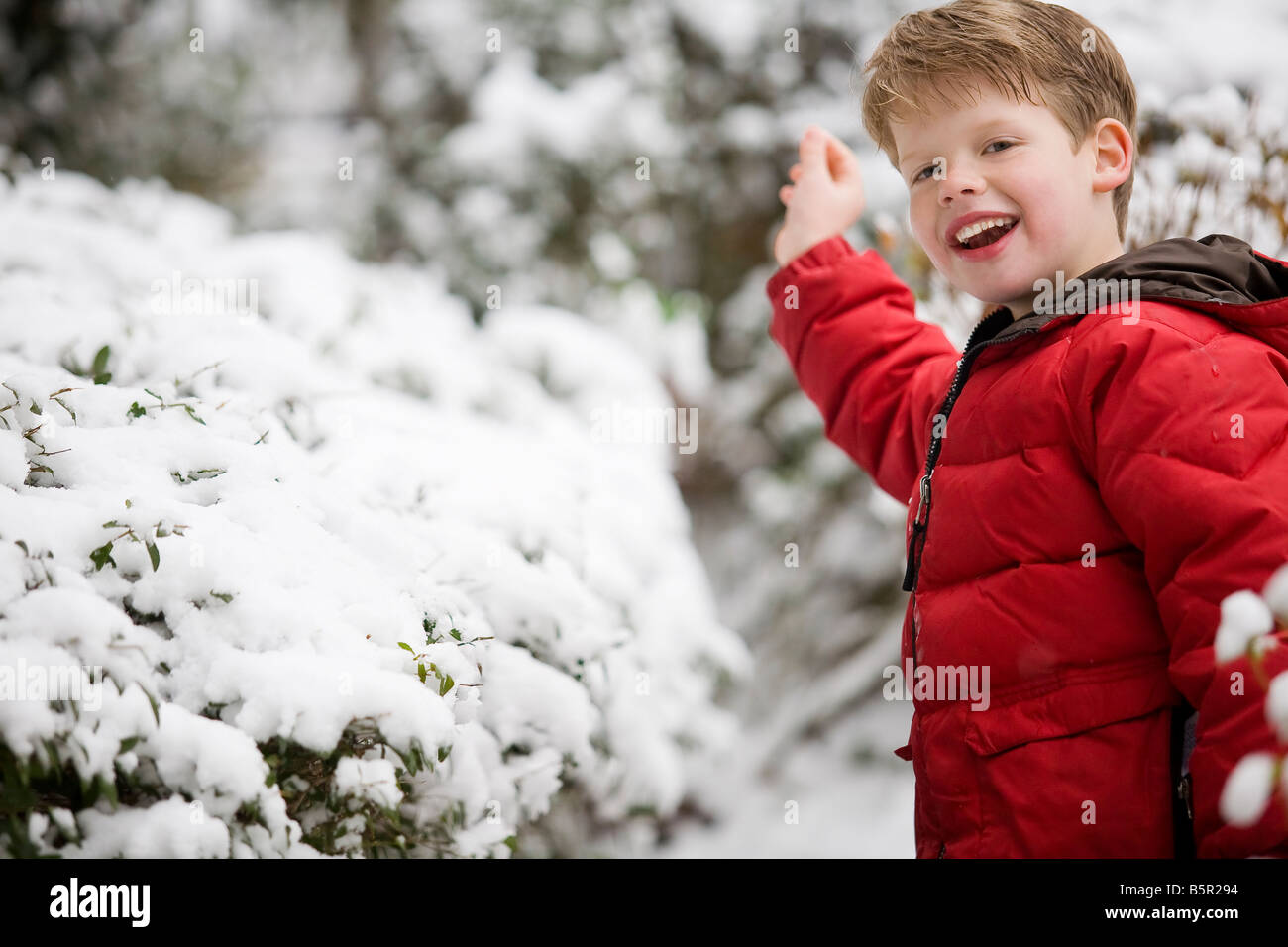 Ragazzo che indossa un rosso goose down jacket sorridente alla fotocamera e a giocare al di fuori nella neve. Foto Stock