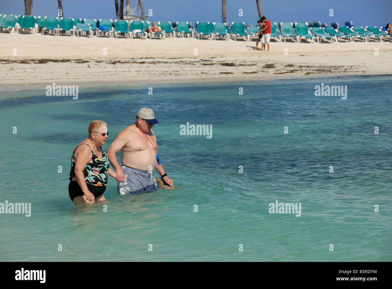 Una coppia matura venture nell'oceano insieme tenendo le mani a poco Staffili Cay, Bahamas. Foto Stock